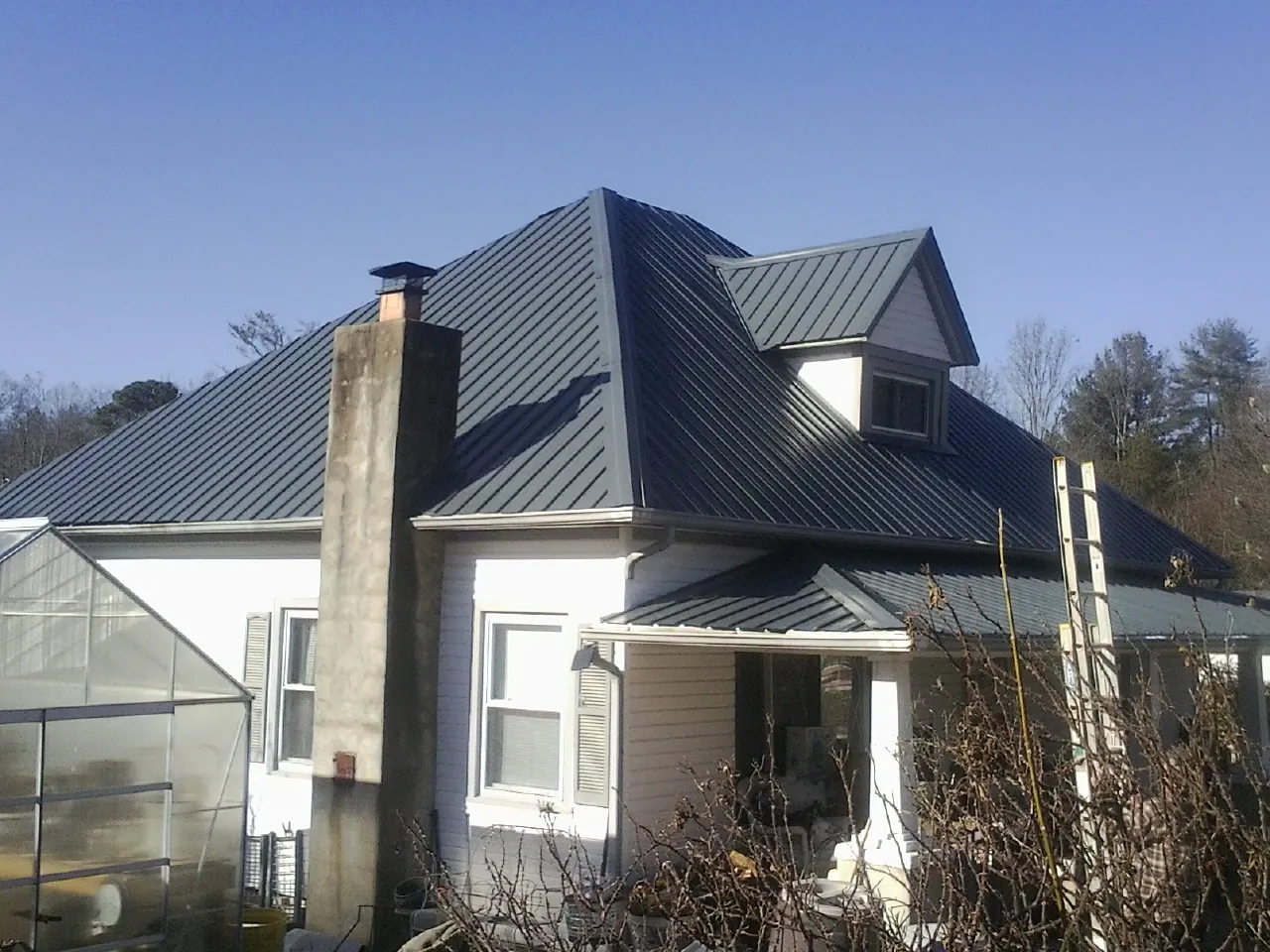 Dark blue standing seam metal roof on a white farmhouse with dormer — Slate & Tile Roof Repair by Roofing Brothers in Dillon
