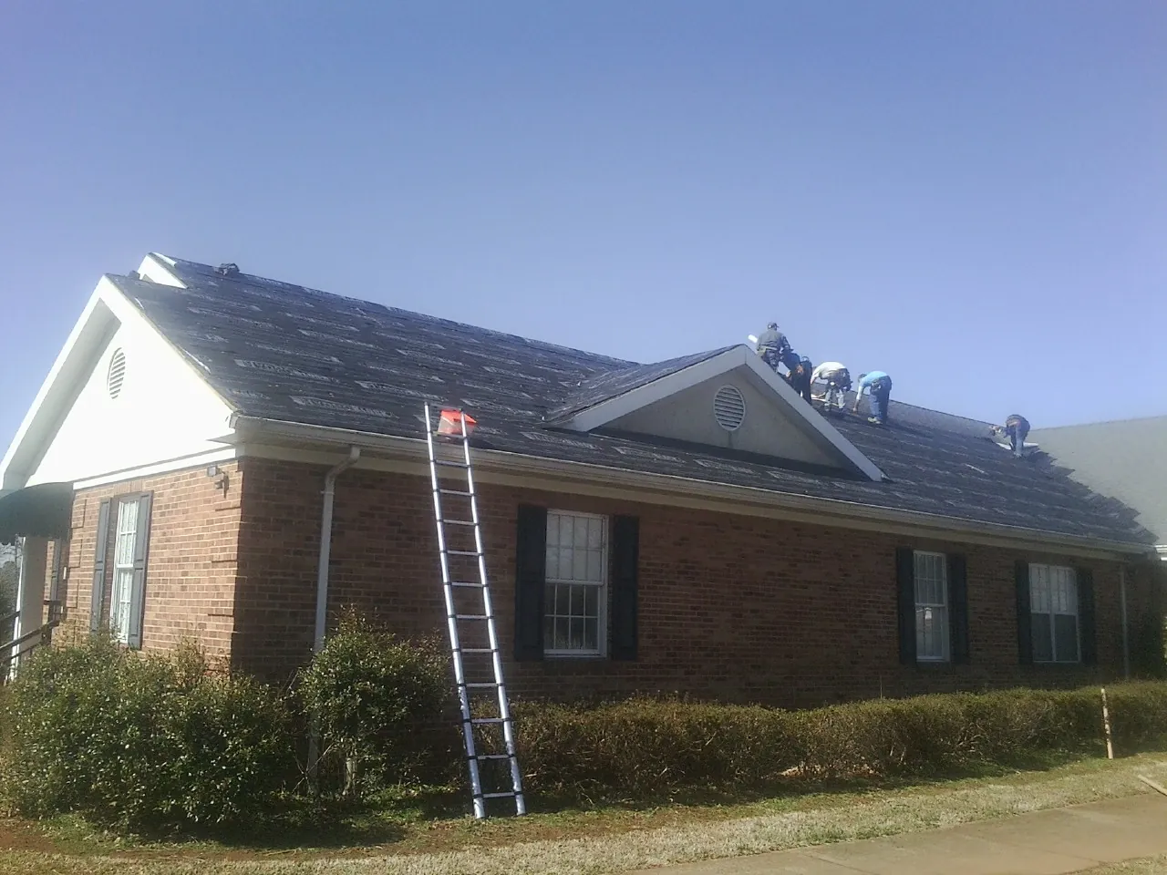 Crew tearing shingles off a brick ranch roof with a ladder set — Emergency Roof Repair work by our crew in Dillon