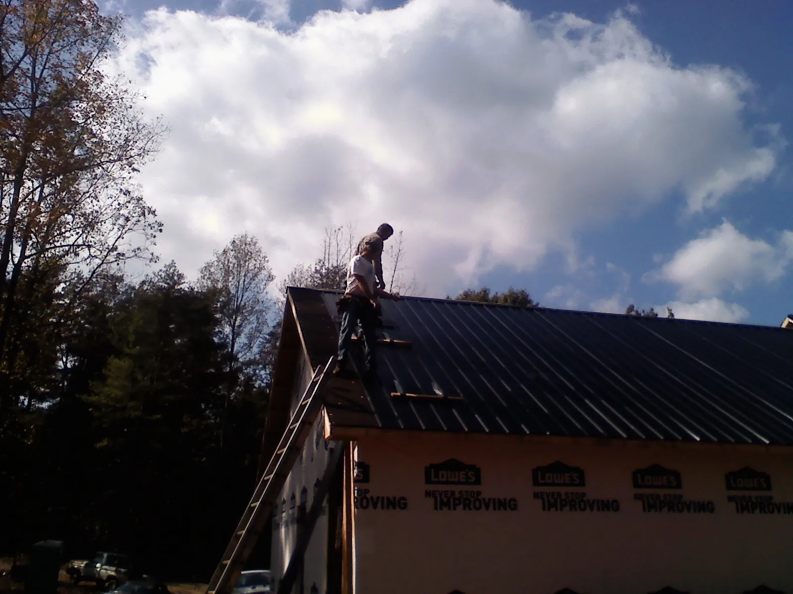 Roofer fastening dark metal panels high against a cloudy sky, from a Roof Inspection job in Dillon