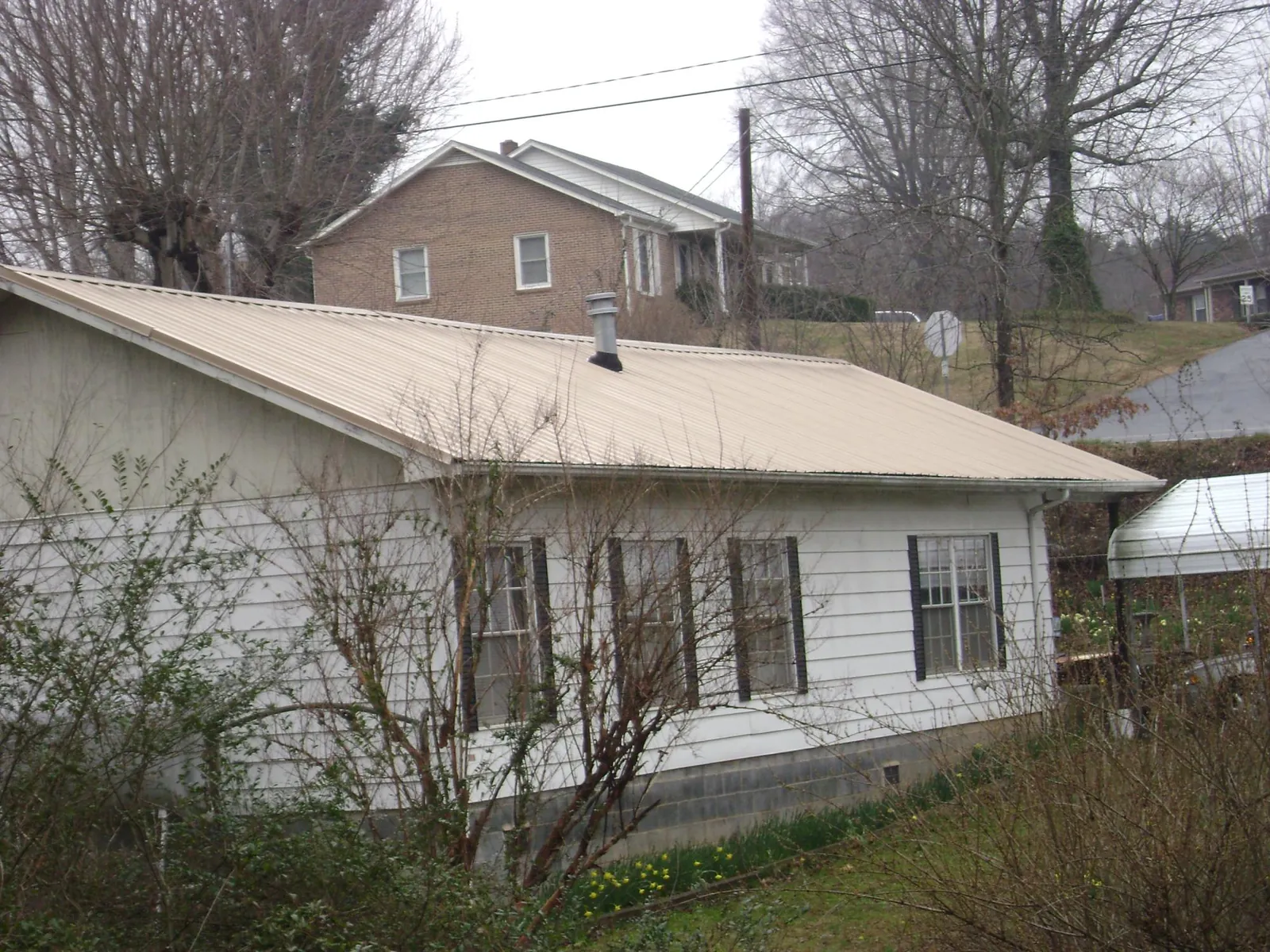 Tan metal roof on a white sided house set into a hillside — Commercial Roofing by Roofing Brothers in Dillon